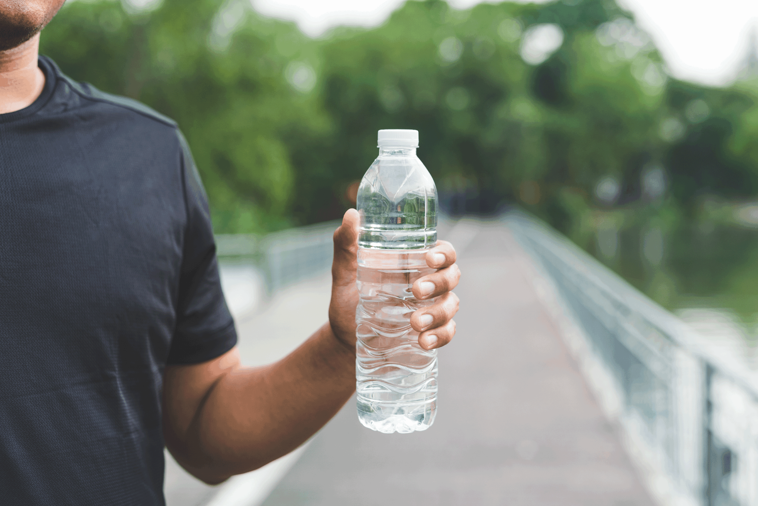 A person holds a water bottle on a park trail.